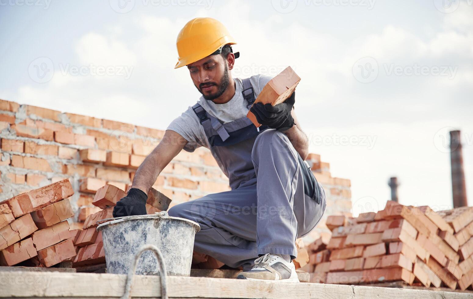 Bucke,t on ,the ground, holding a brick. Handsome Indian man is on the construction site photo