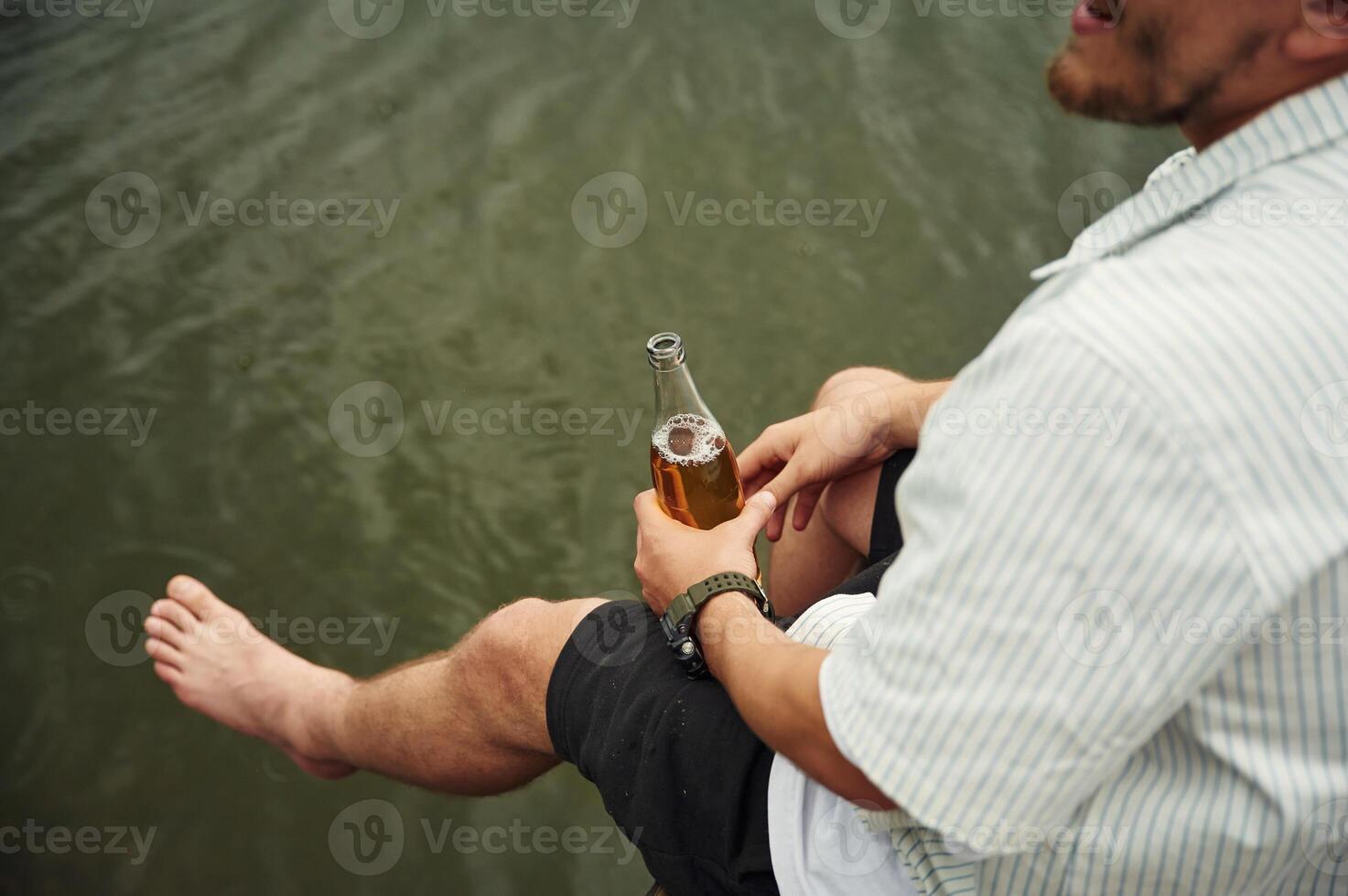 Close, up, view of man that is sitting by the water with beer in hands photo