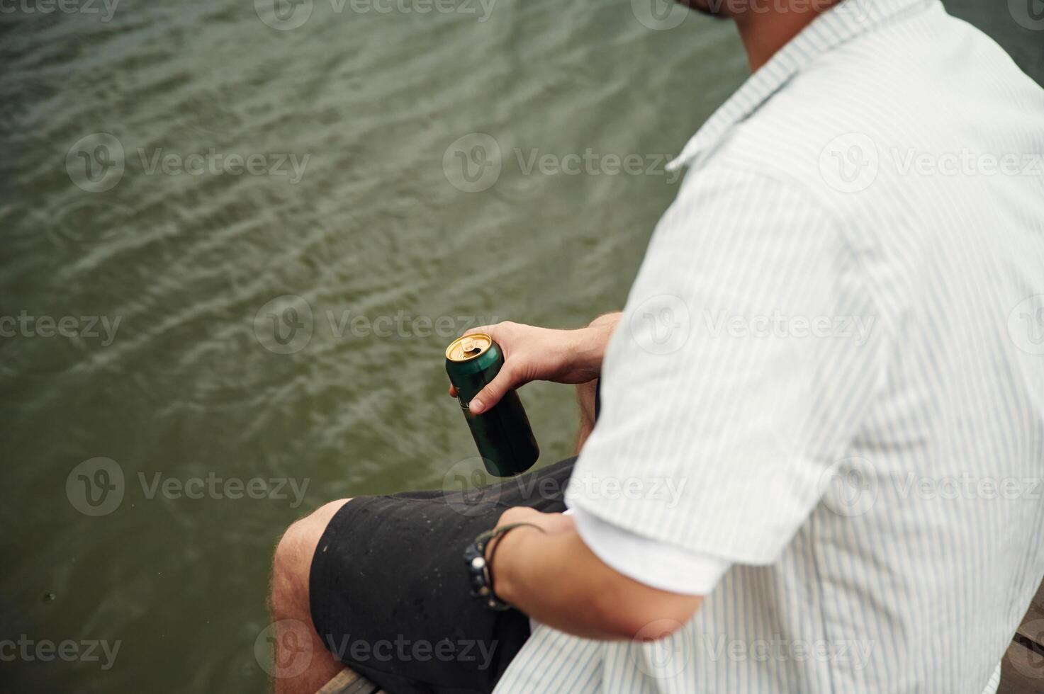Close up view ,of man that is sitting by the water with beer in hands photo