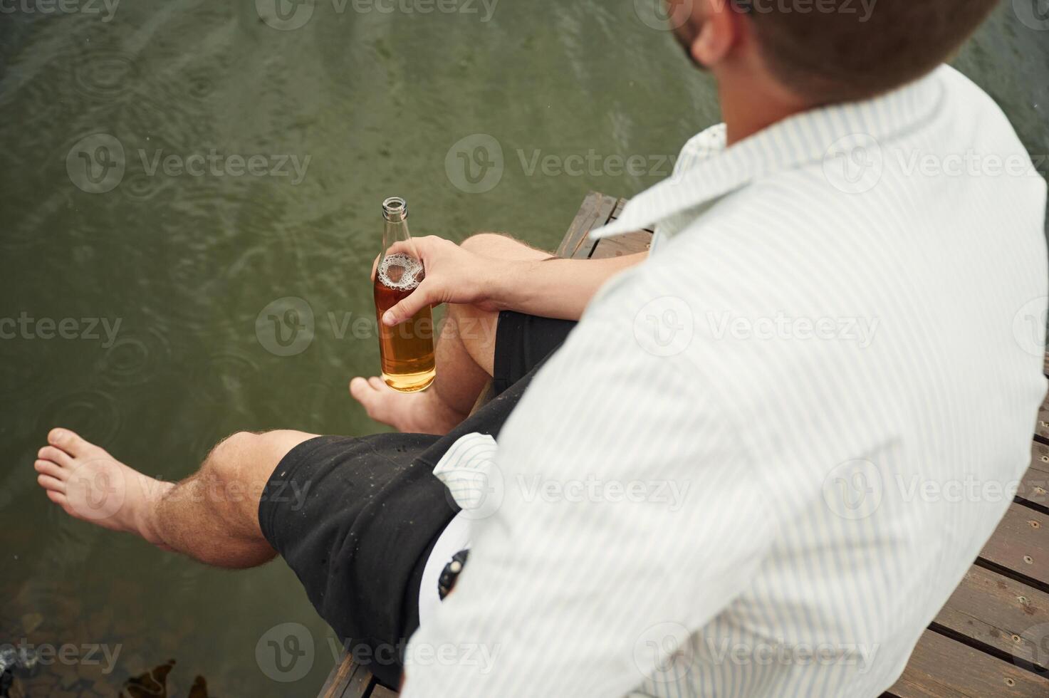 Close ,up view of man that is sitting by the water with beer in hands photo