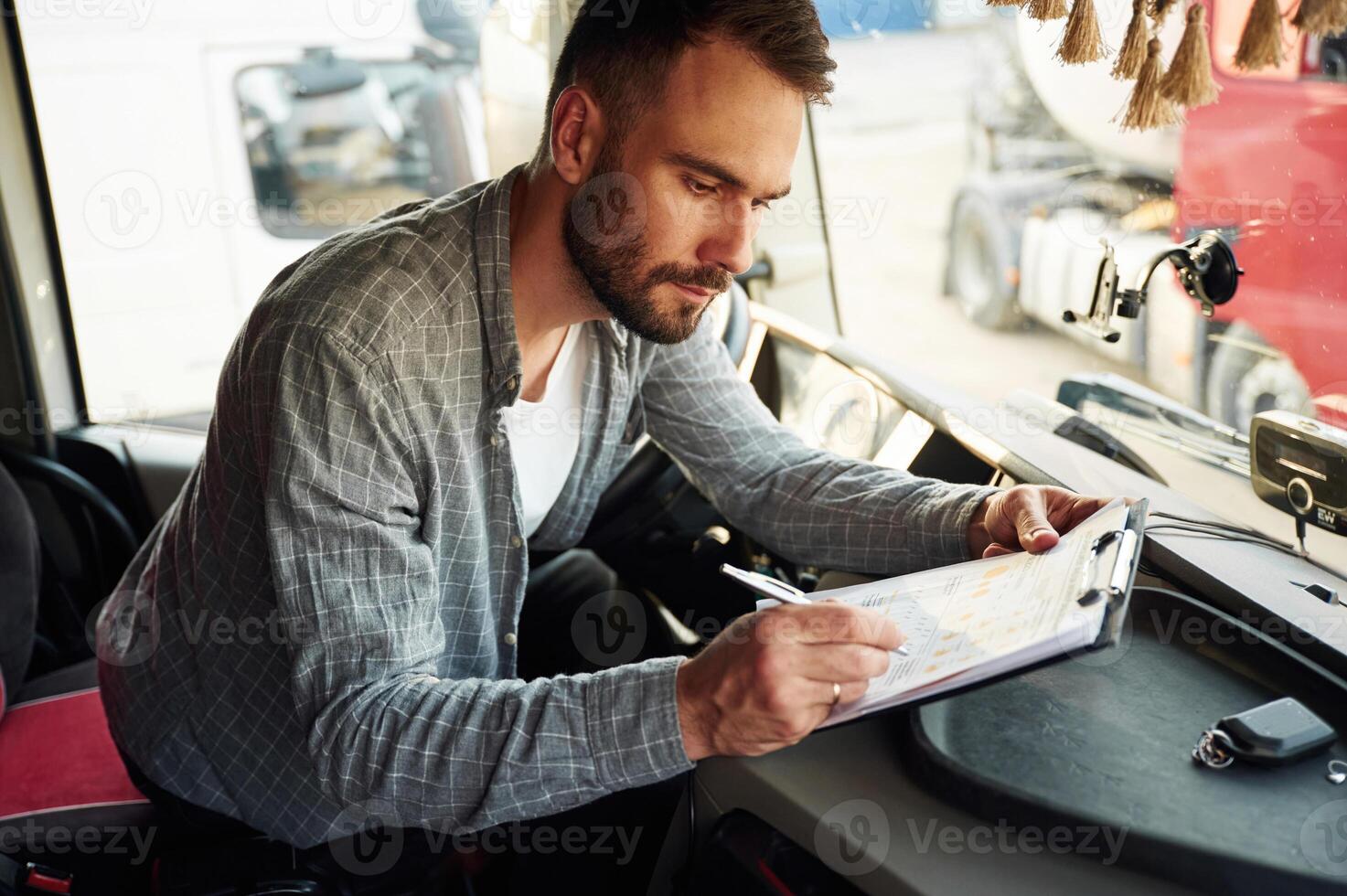 Writing in the document, sitting inside. Young truck driver in casual clothes photo