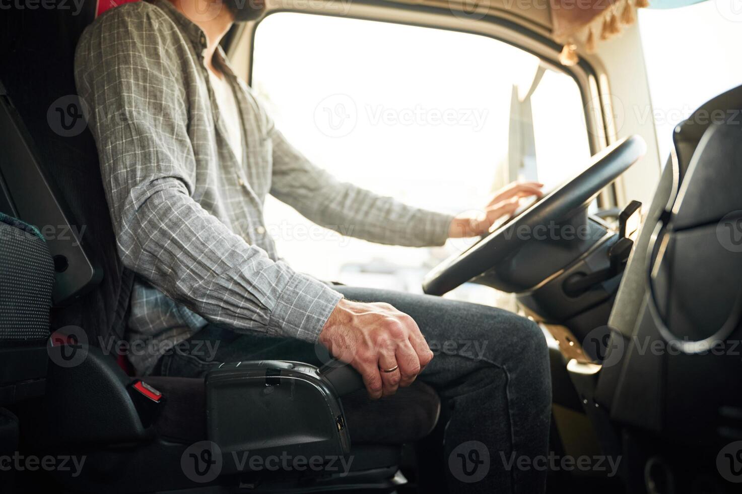 Side, view, sitting inside the vehicle. Young truck driver in casual clothes photo
