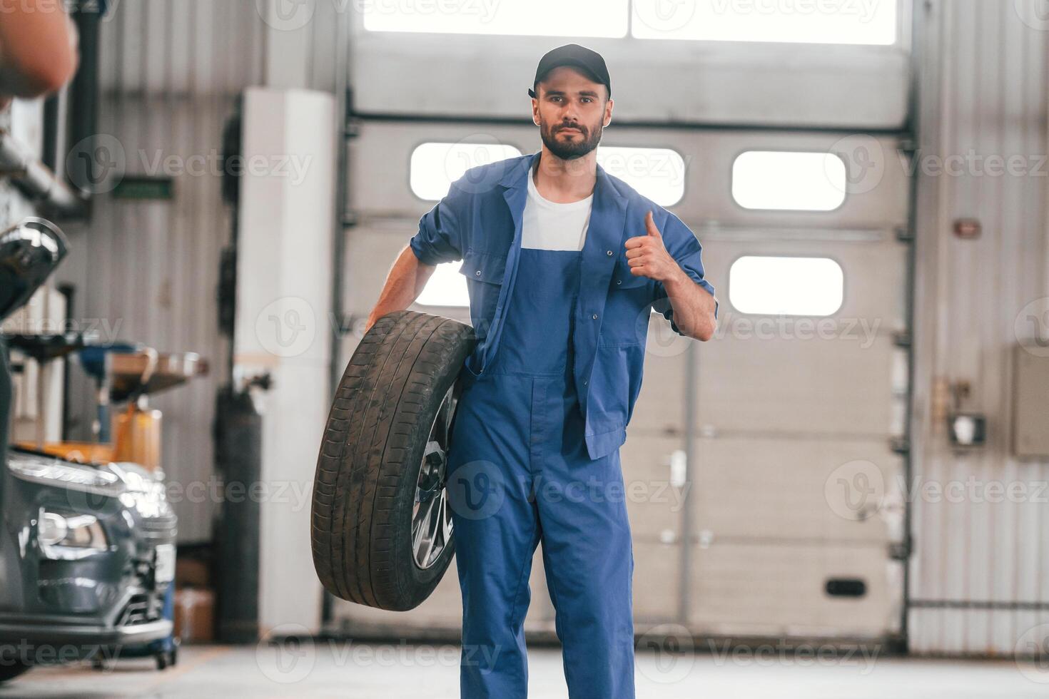 Front view, standing and holding tire. Auto ,mechanic working in garage. Repair service photo