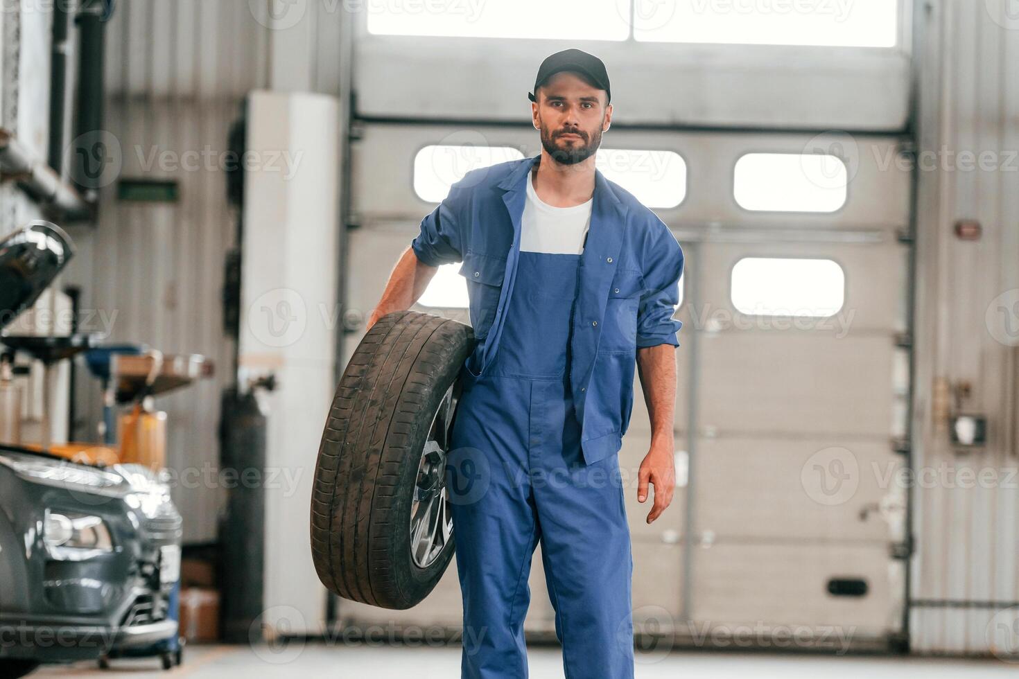 Front view, standing, and holding, tire. Auto mechanic working in garage. Repair service photo
