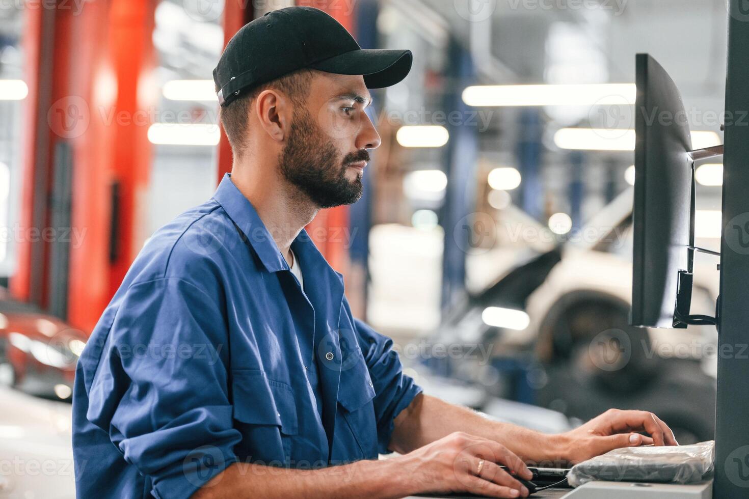 In black ,cap. Using, computer. Auto mechanic working in garage. Repair service photo