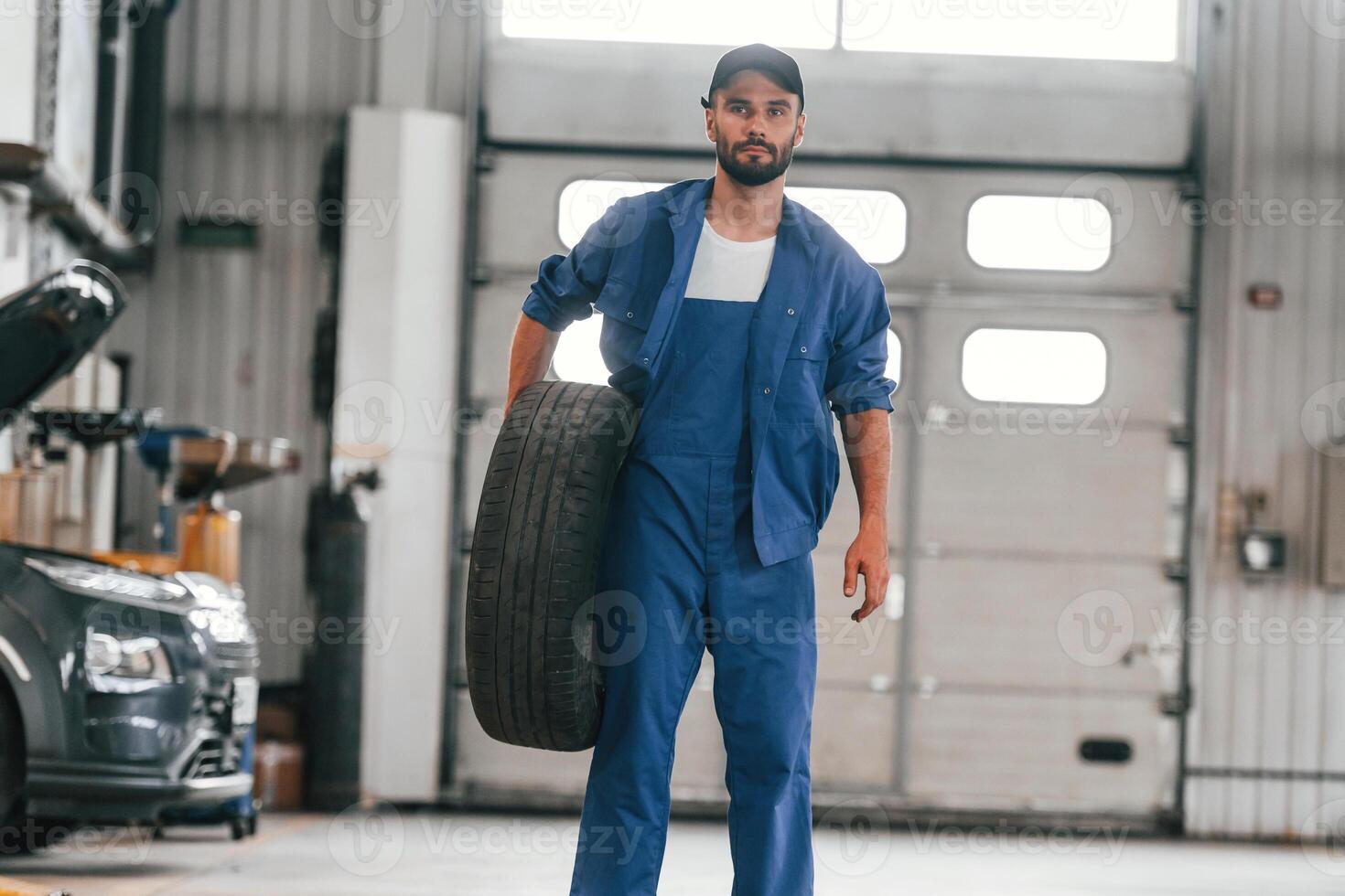 Front view, standing and holding, tire. Auto mechanic working in garage. Repair service photo
