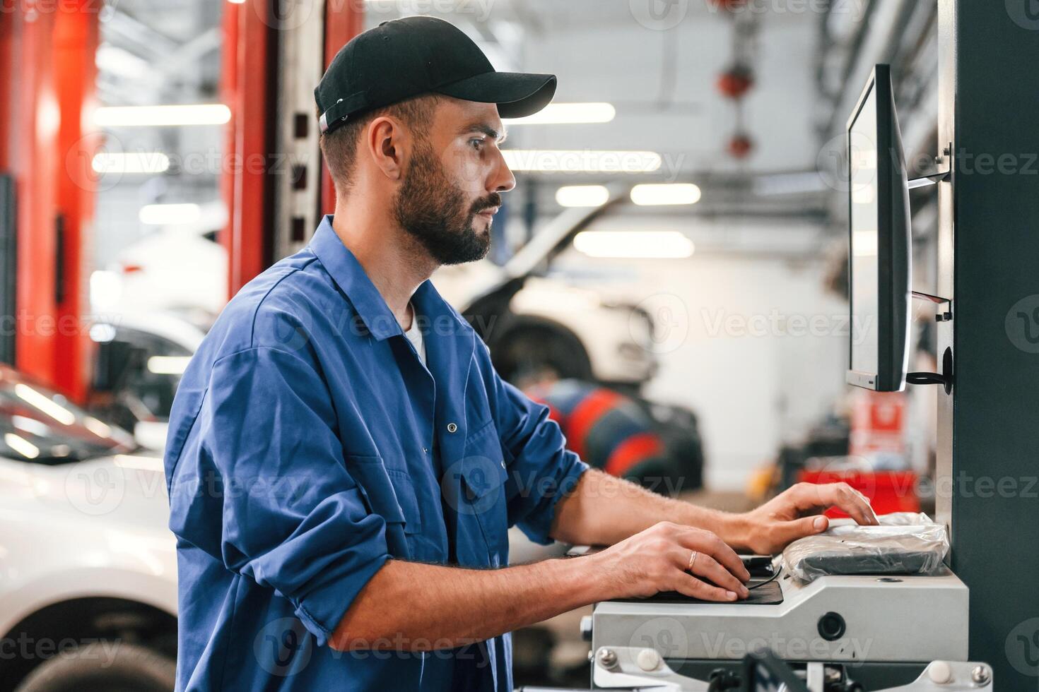 In black cap. Using computer., Auto mechanic working in garage. Repair service photo