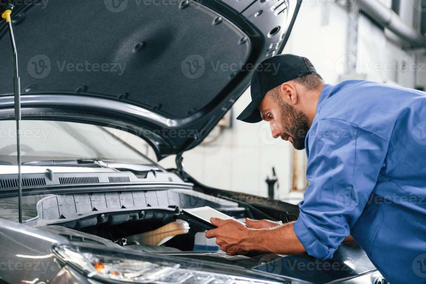 With tablet in hands.. Auto mechanic working in garage. Repair service photo