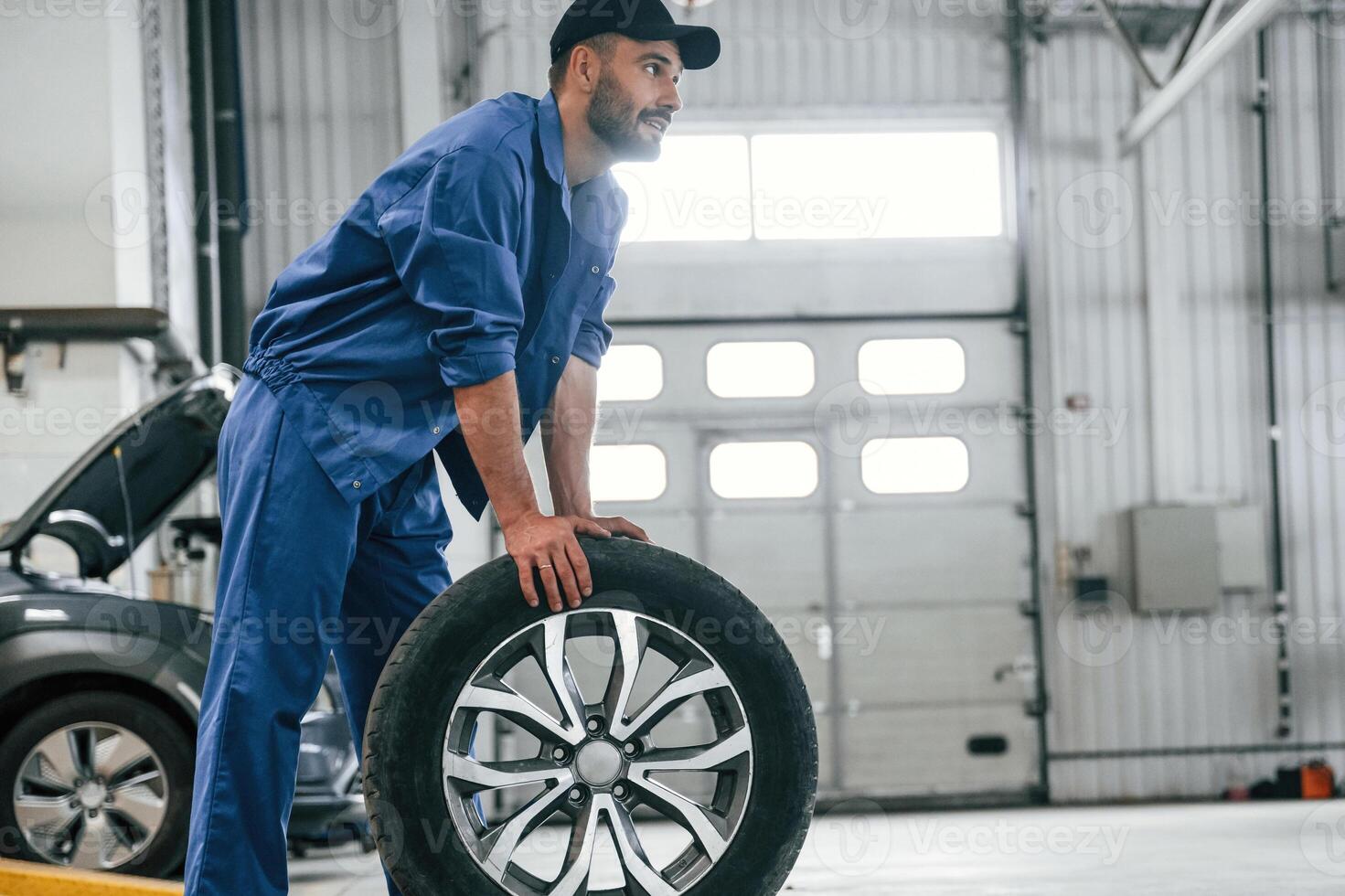 New tire, moving it. Auto mechanic working in garage. Repair service photo