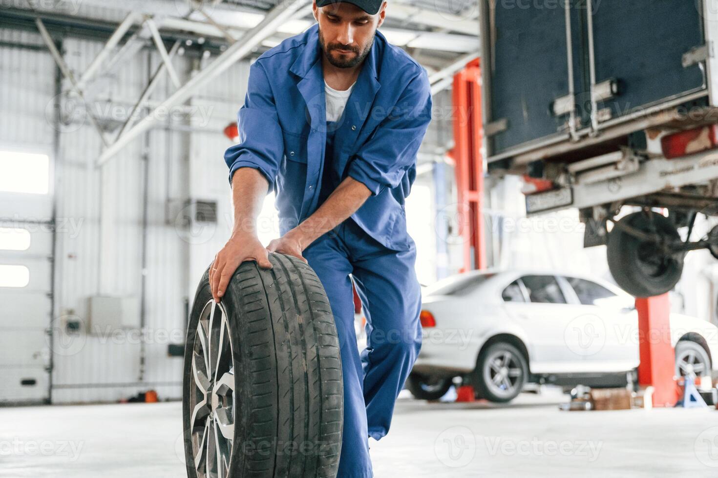 Walking forward, with new, tire. Auto mechanic working in garage. Repair service photo