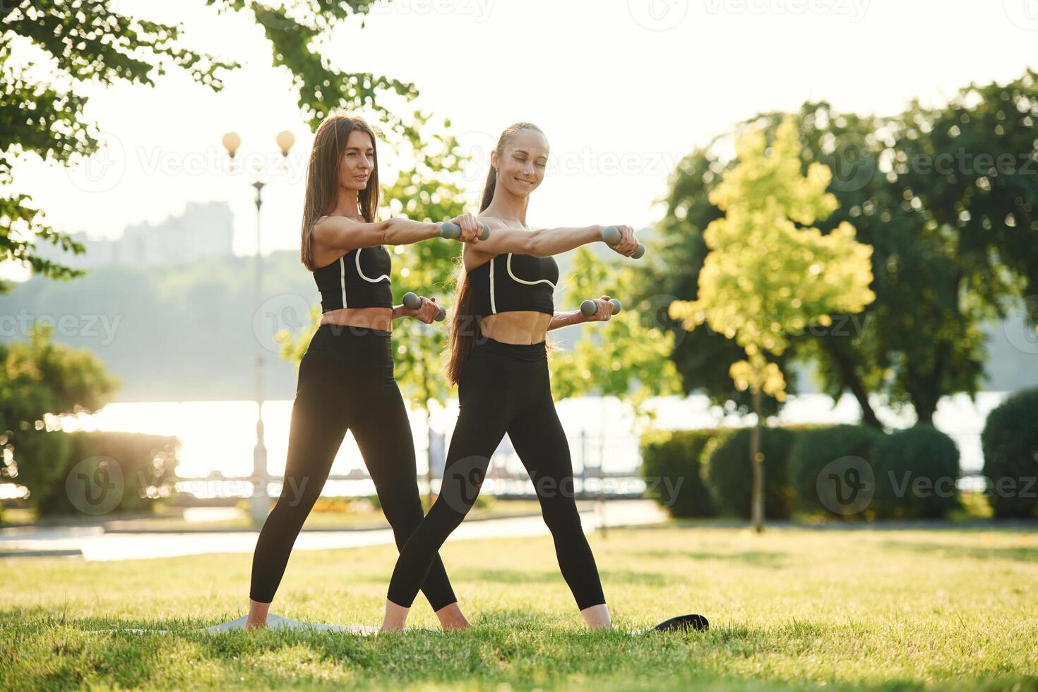 With ,dumbbells.. Two women in sport clothes are doing exercises outdoors on the field photo
