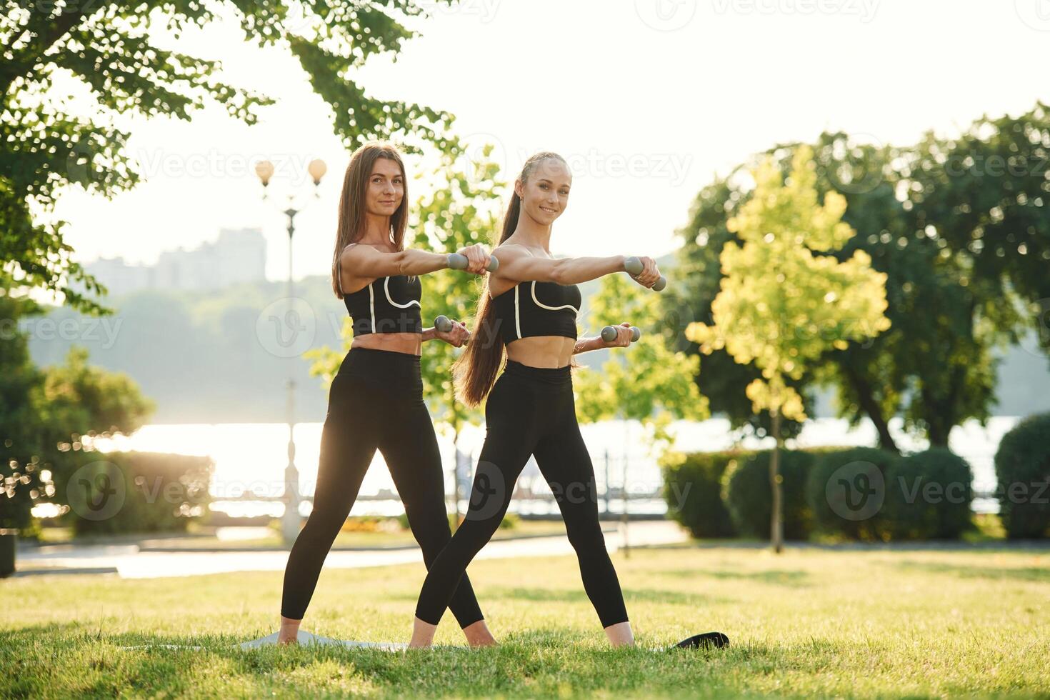 Dumbbells in hands.. Two women in sport clothes are doing exercises outdoors on the field photo