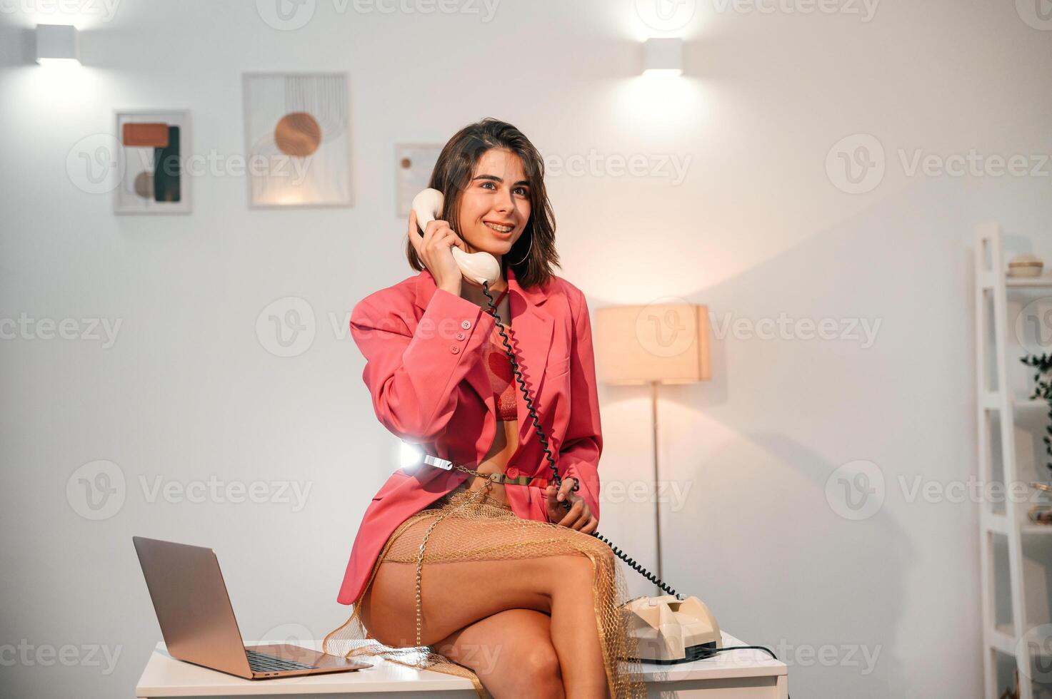 Sitting on the ,table and talking by retro ,old phone. Woman in red clothes is indoors in the domestic room photo