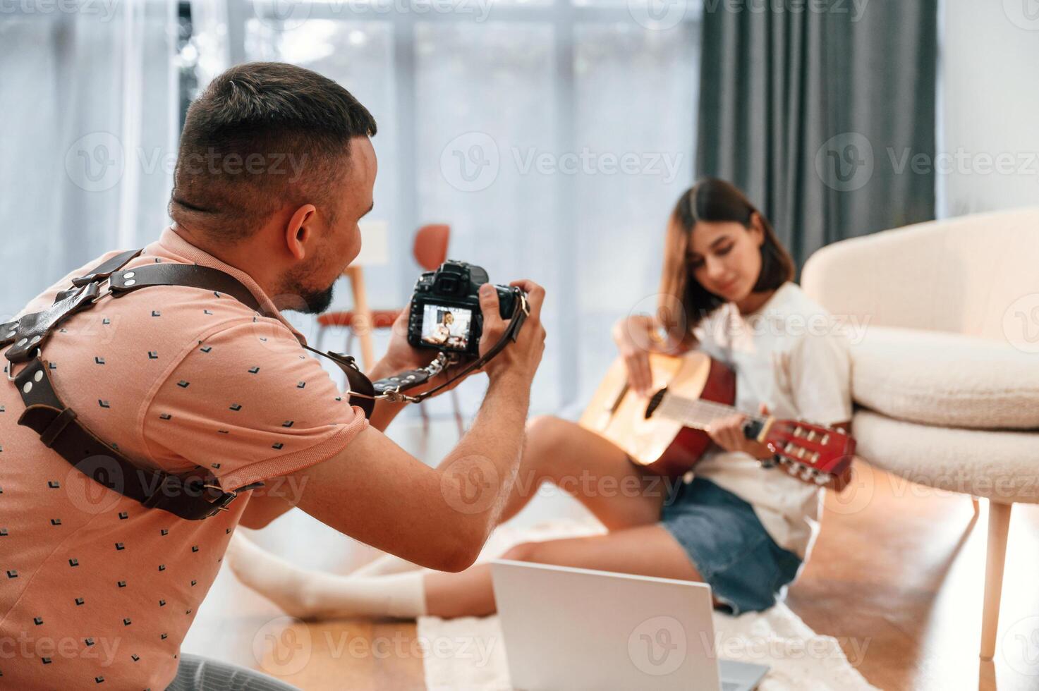 Photographer is ,working, using camera. Beautiful woman in casual clothes is at home with guitar photo