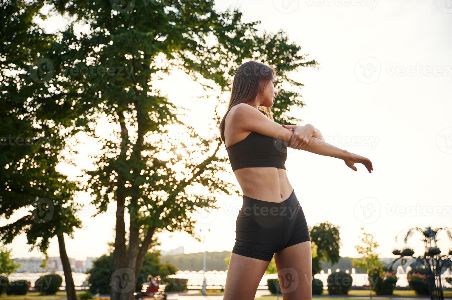 Exercises,, against, tree and sky. Beautiful young woman in sportive clothes is in the park at sunny daytime photo
