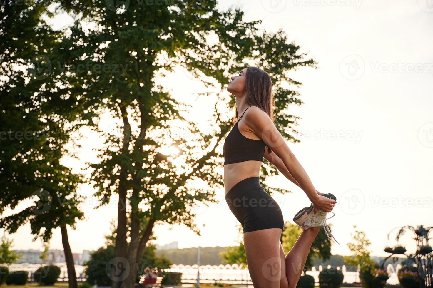 Exercises, ,against tree and sky. Beautiful young woman in sportive clothes is in the park at sunny daytime photo