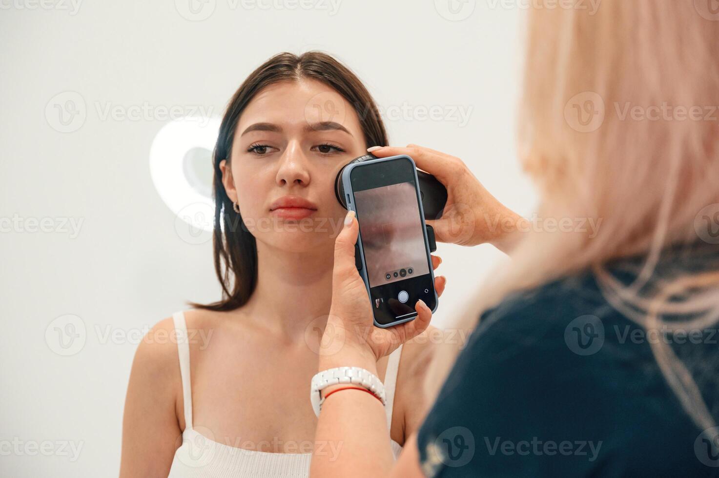 Using smartphone. Getting photo rejuvenation procedure at cosmetology clinic. Women in beauty salon