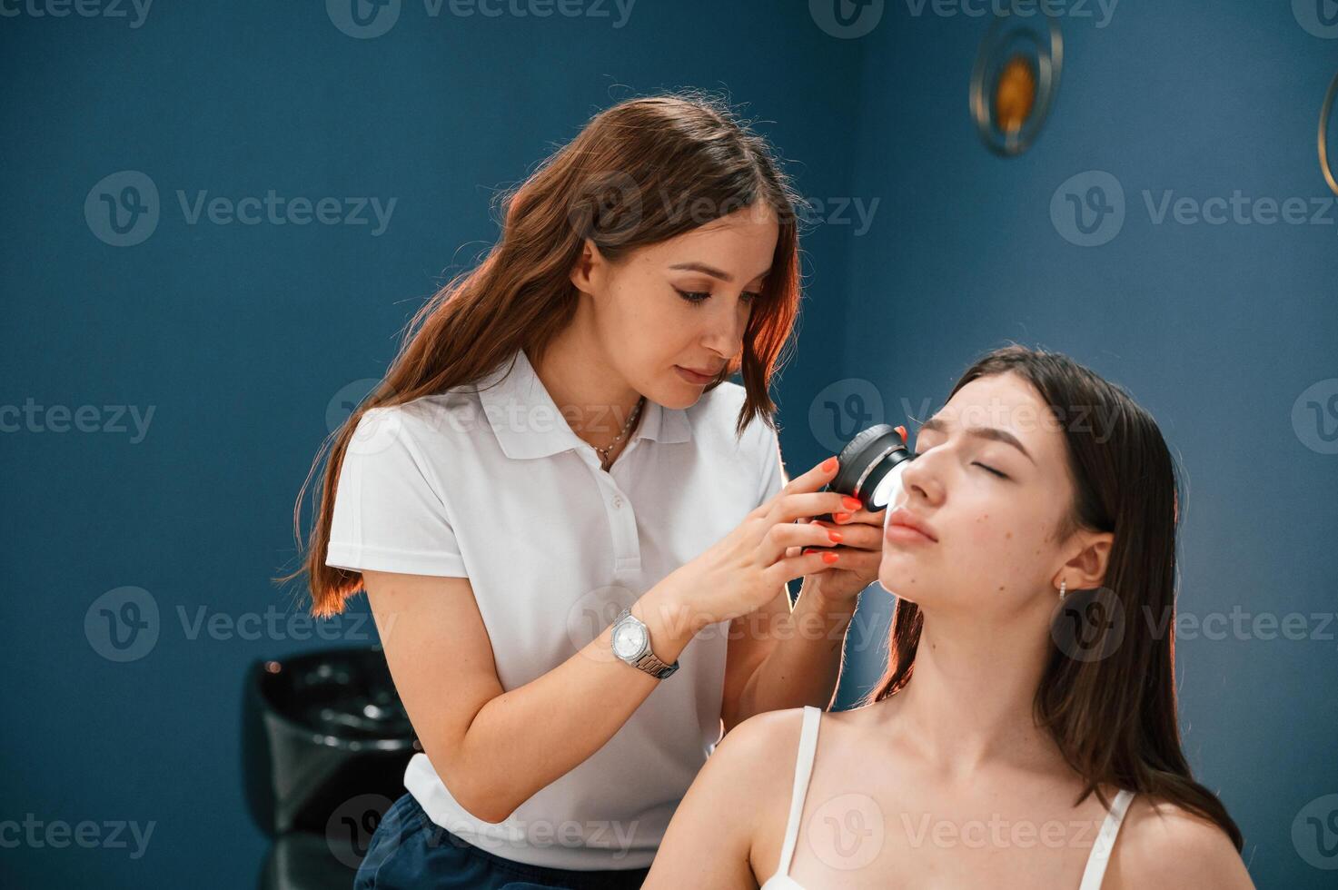 Beauty ,salon ,worker is examining skin of the woman by using a device with light and lens photo
