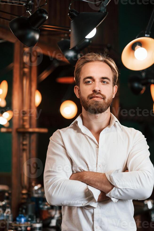 Standing with arms ,crossed. Handsome barber is in the salon photo