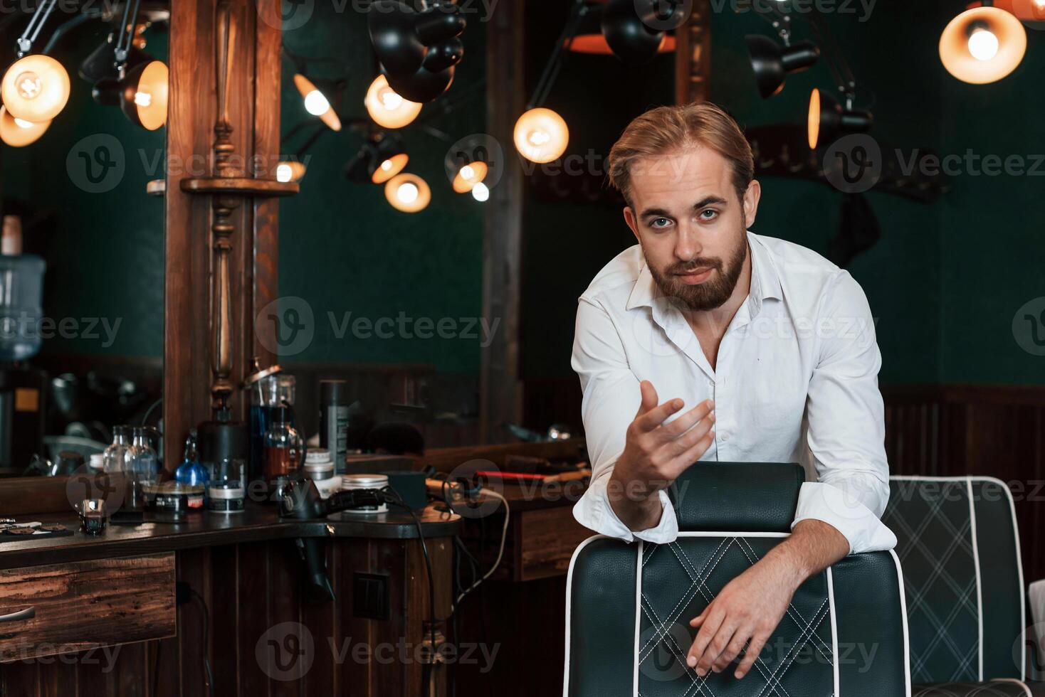 Leaning on the chair. .Handsome barber is in the salon photo