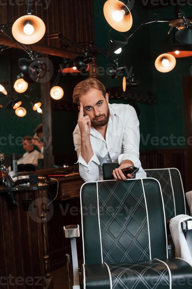 Leaning on th,,e chair. Handsome barber is in the salon photo