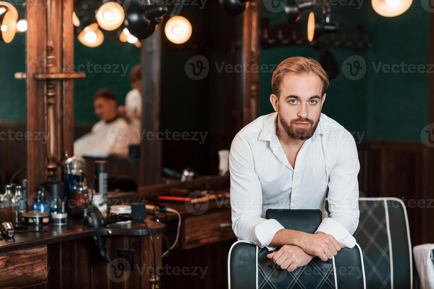 Leaning ,on the chair. Handsome barber is in the salon photo