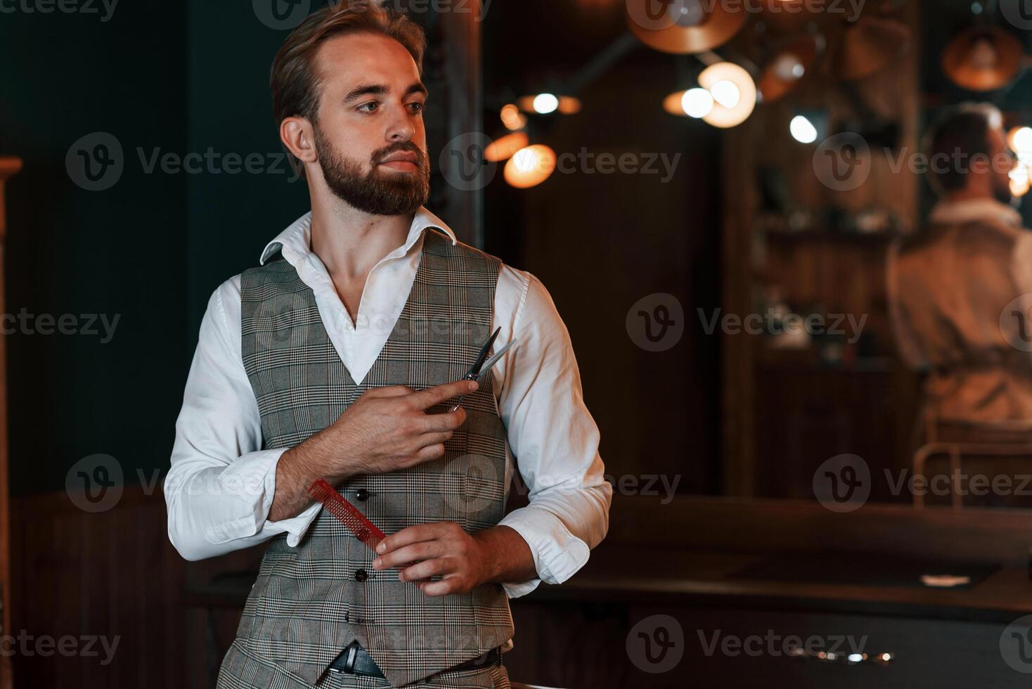 Standing,, holding equipment. Handsome barber is in the salon photo