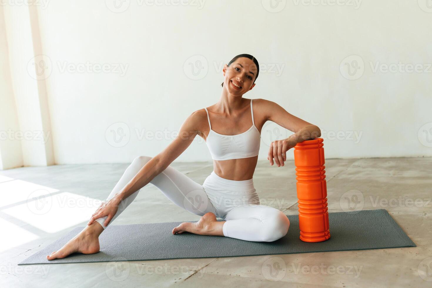 With orange colored foam roller., Young woman with slim body type is in fitness clothes in the studio photo