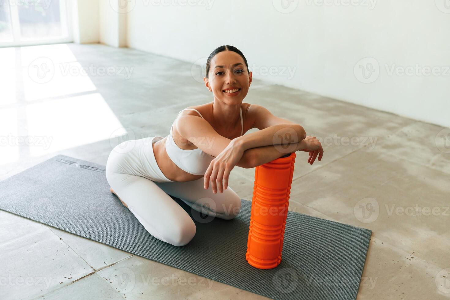 Sitting with, foam roller. Young woman with slim body type is in fitness clothes in the studio photo