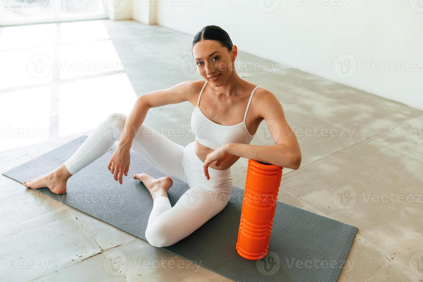Sitting ,with foam roller. Young woman with slim body type is in fitness clothes in the studio photo