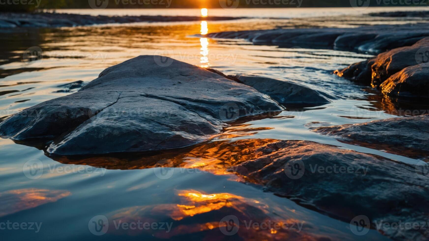 A serene sunset reflecting on water with rocks in the foreground. photo