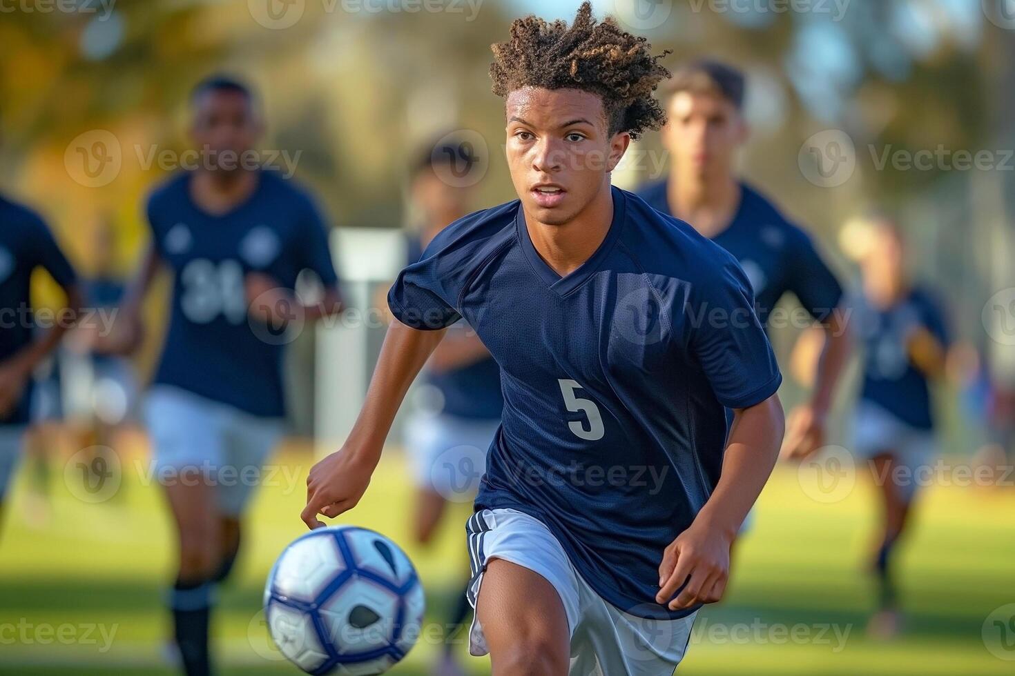 A young Black male soccer player in motion, focused on the ball while teammates support him in the background. photo