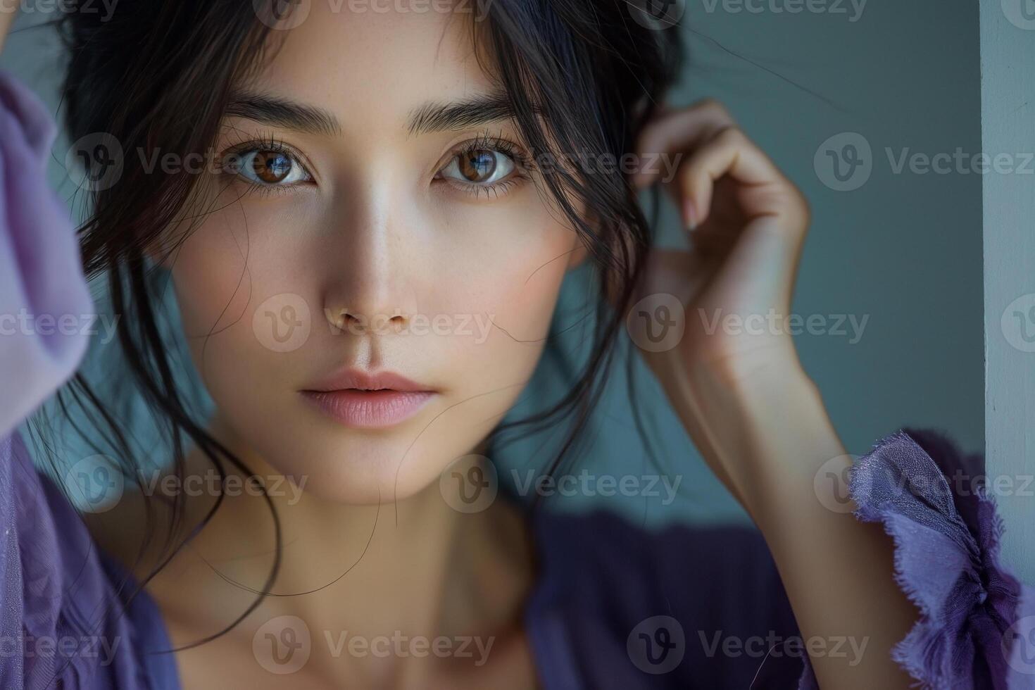 Portrait of a young Asian woman with soft features, wearing a purple blouse, gazing thoughtfully towards the camera with a gentle expression. photo