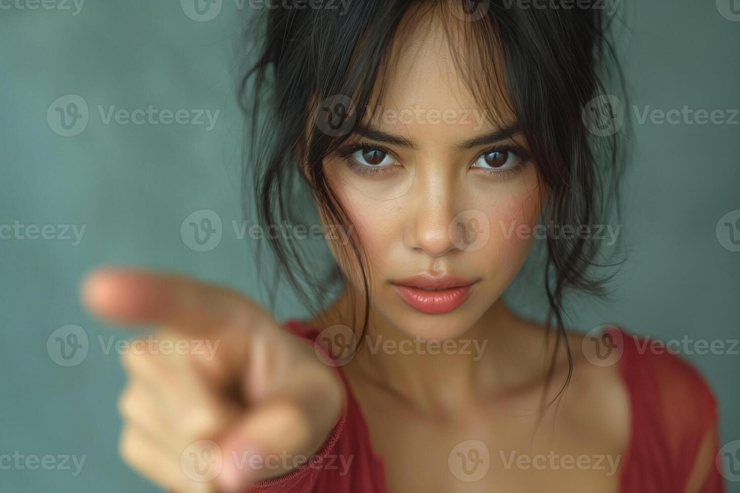 A striking young woman with medium skin tone points assertively at the viewer, showcasing a fierce and determined expression. photo