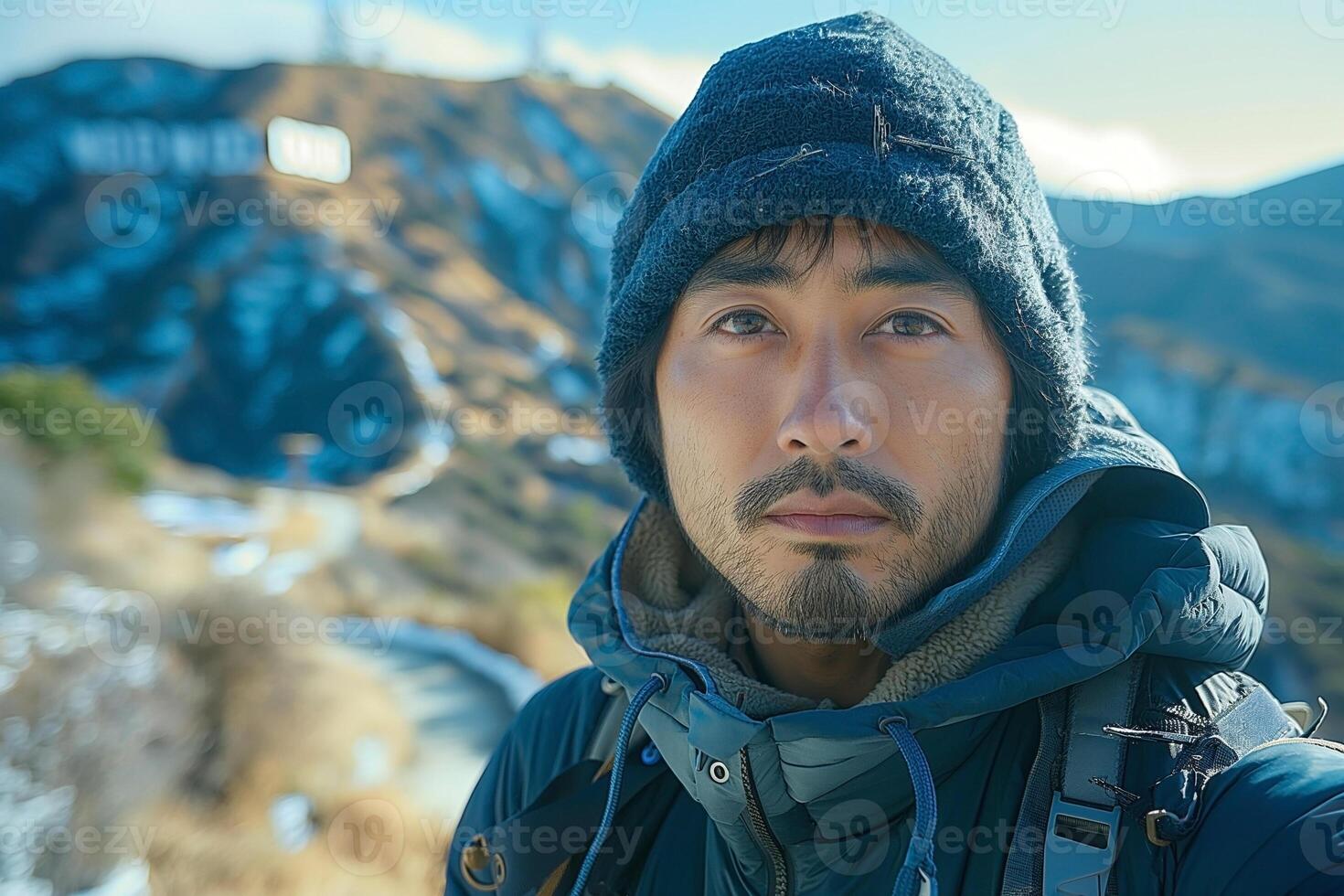 A young Asian male adventurer stands against a scenic backdrop, wearing a warm jacket and beanie, exuding a sense of determination. photo