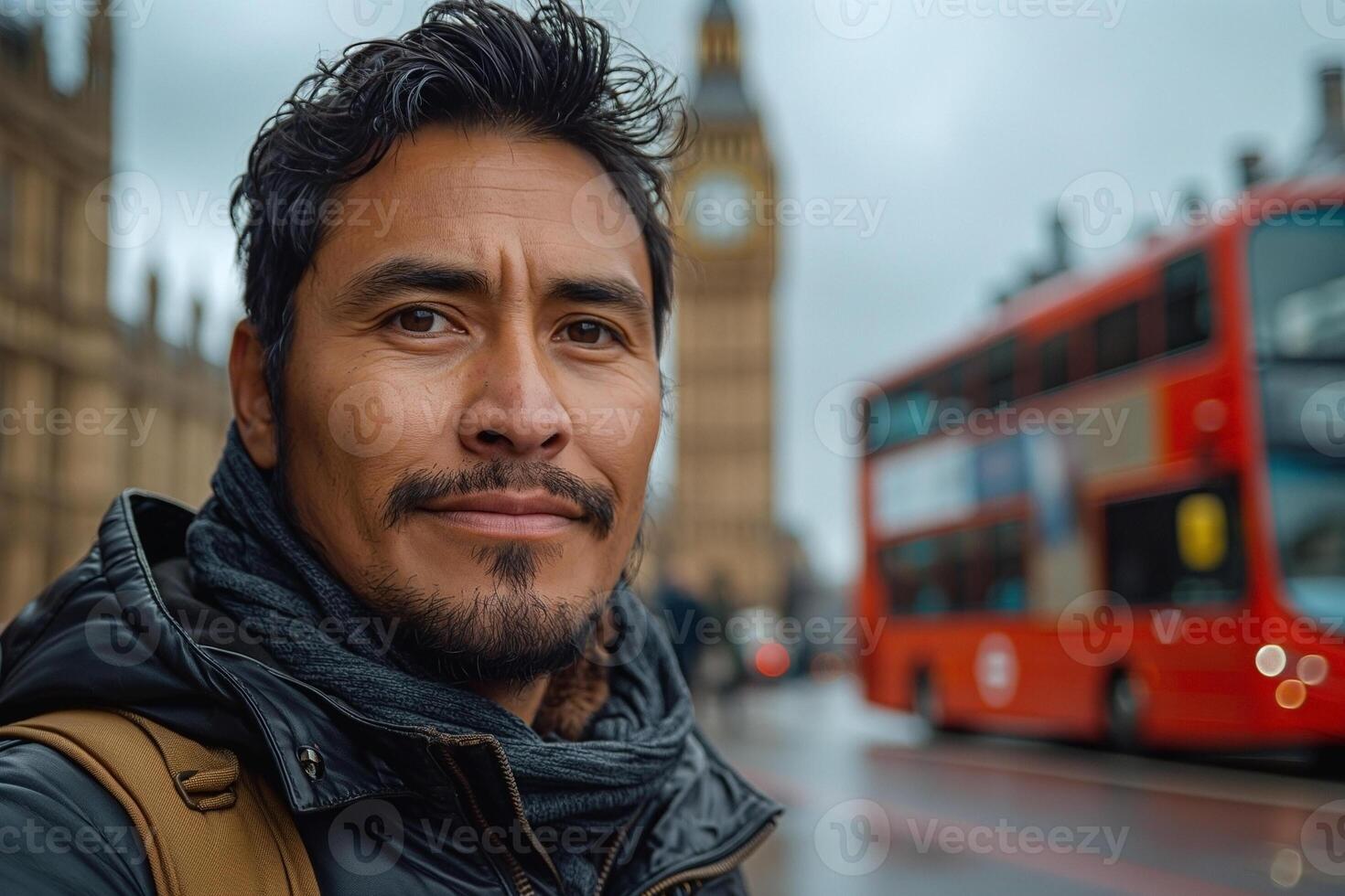 A Hispanic male with a rugged look smiles confidently in front of a London bus and Big Ben on a cloudy day. photo