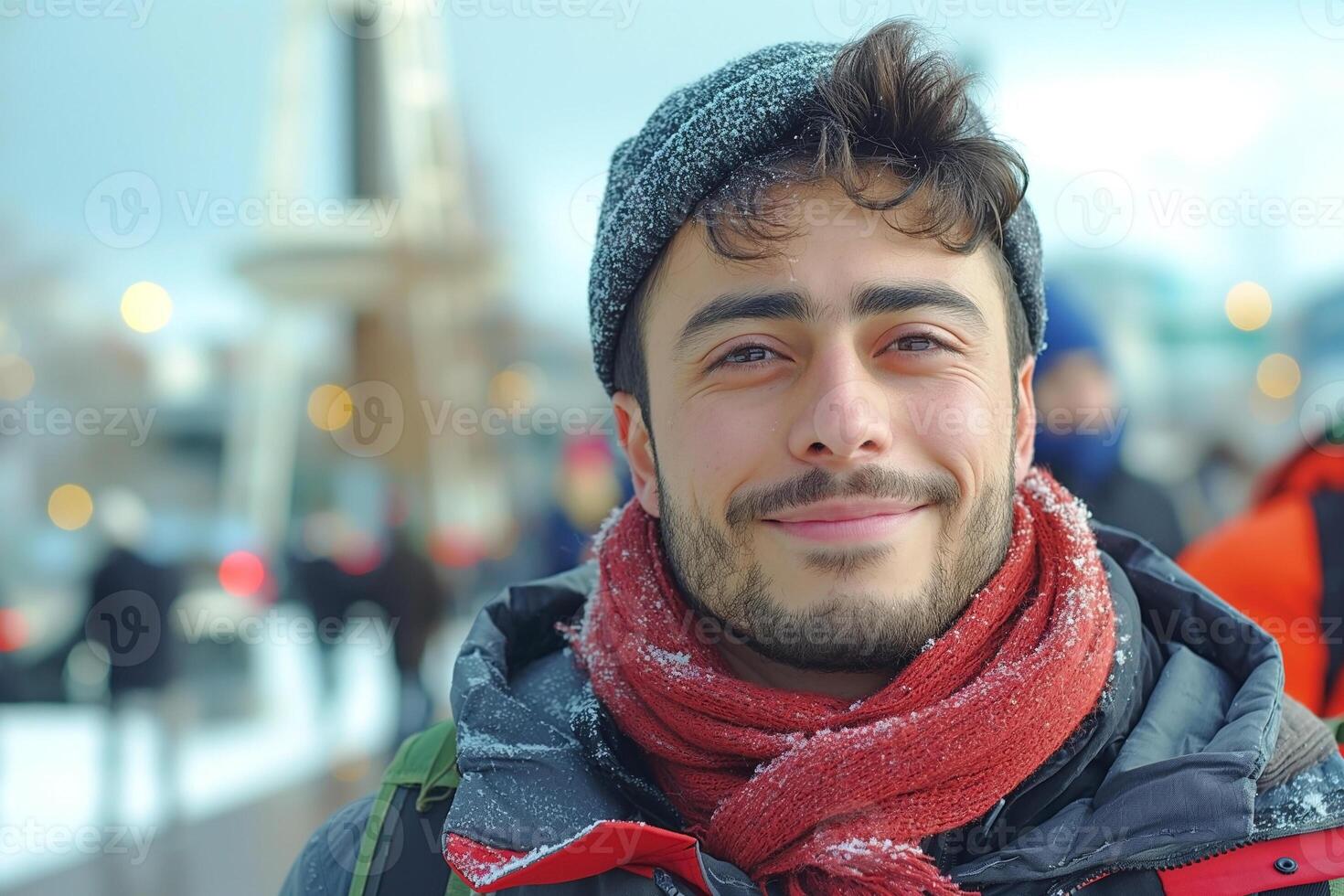 A smiling young man with tousled hair wearing a gray beanie and red scarf, surrounded by a wintery backdrop. photo