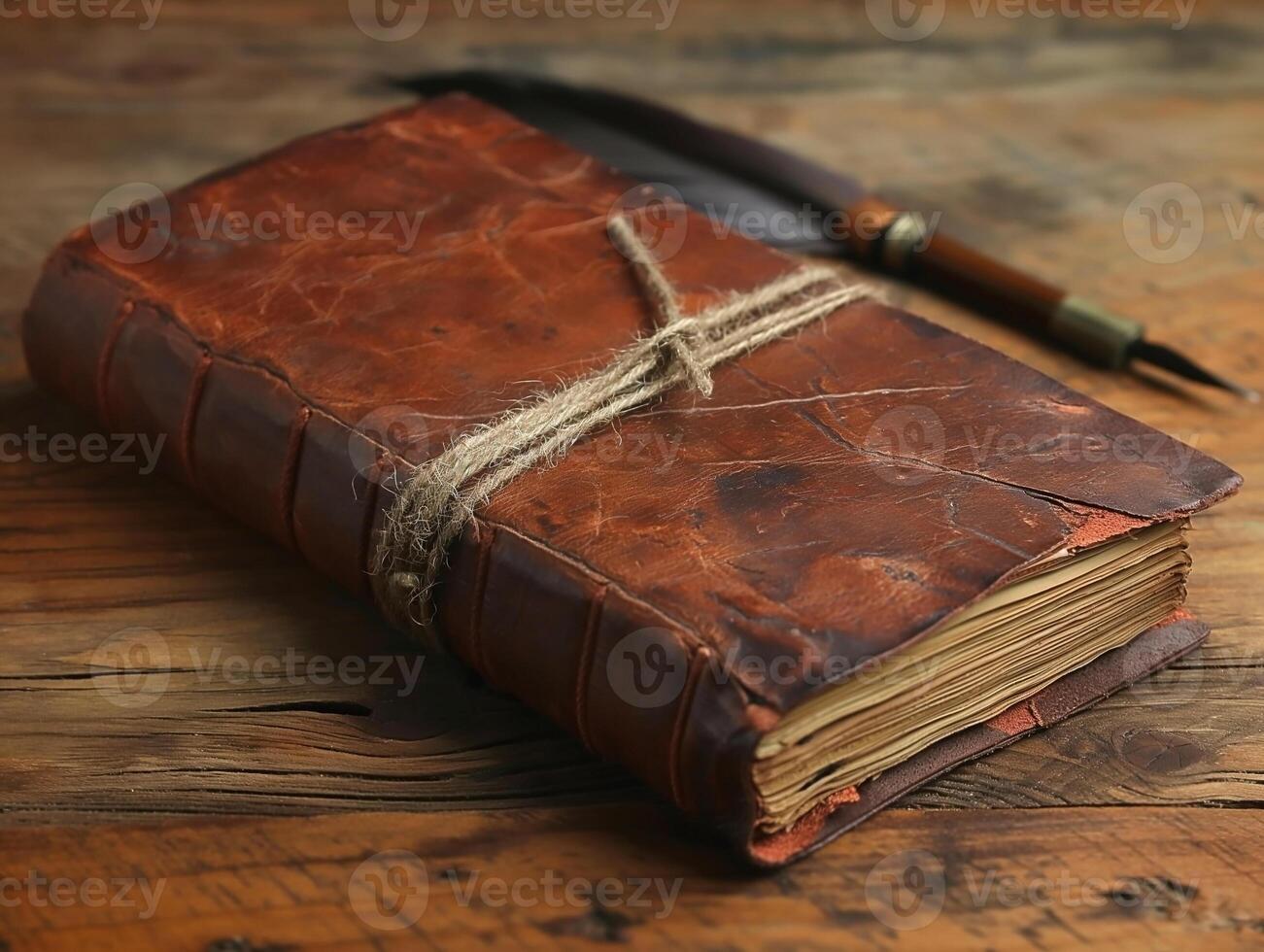 A vintage brown leather-bound journal tied with twine, accompanied by a classic quill pen on a rustic wooden surface. photo