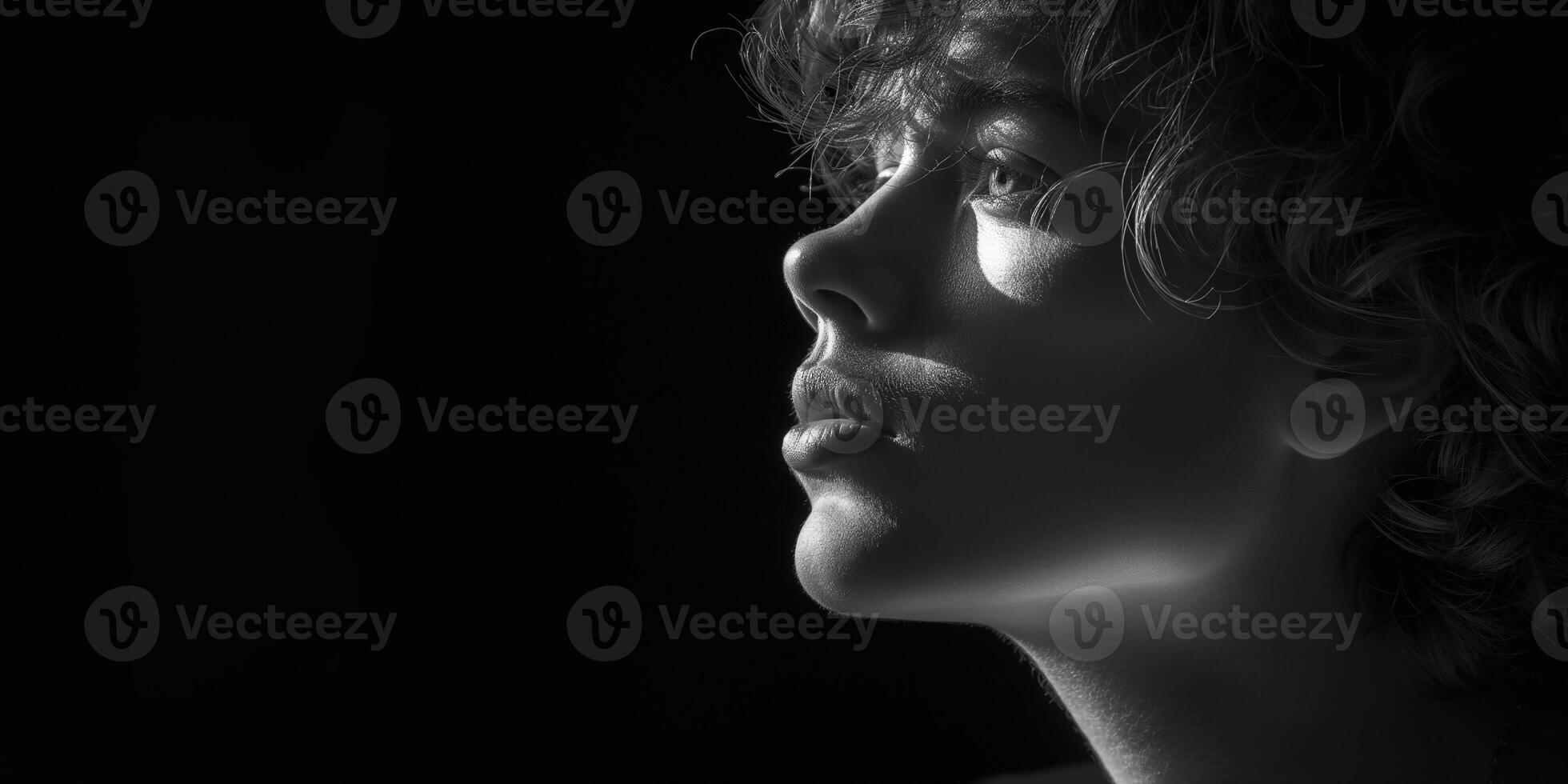 Close-up profile of a young Caucasian male with curly hair, captured in dramatic black and white lighting. photo