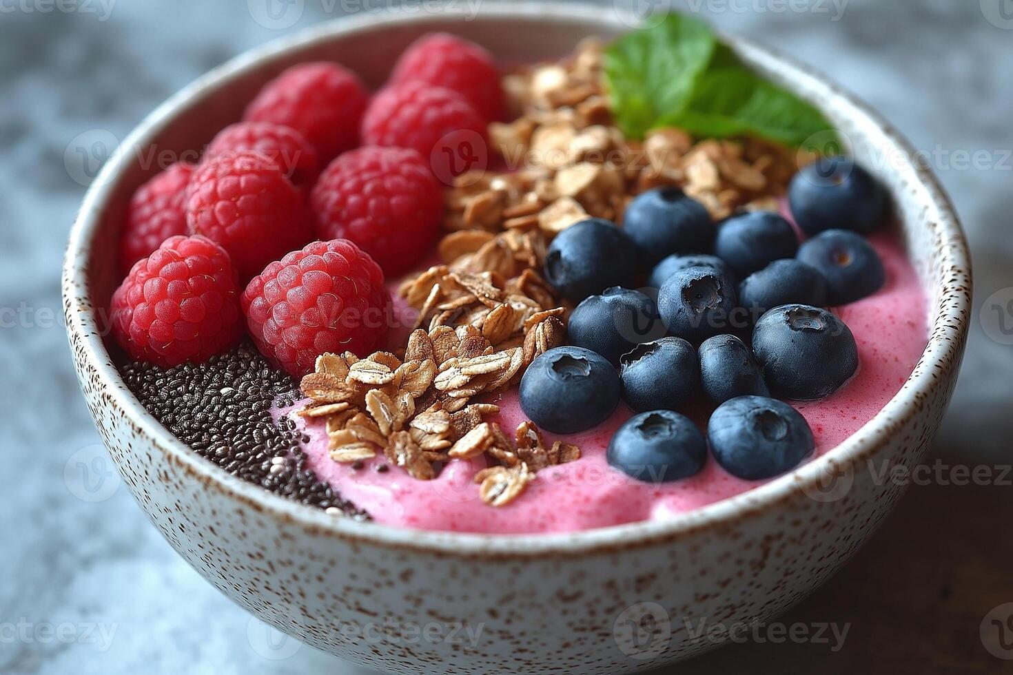 A beautiful bowl of vibrant smoothie topped with fresh blueberries, raspberries, granola, chia seeds, and a sprig of mint. photo