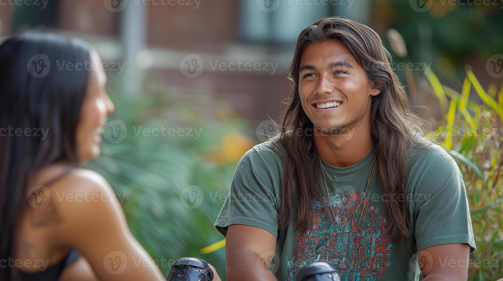 A cheerful young man of mixed heritage shares a laugh with a friend outdoors, surrounded by lush greenery. photo