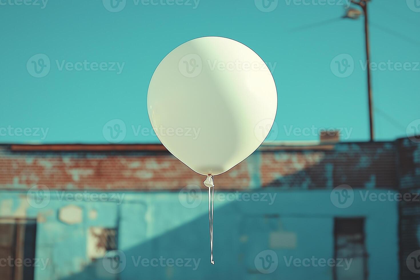 A single white balloon gently floats against a vibrant blue sky backdrop, evoking a sense of nostalgia and whimsy. photo
