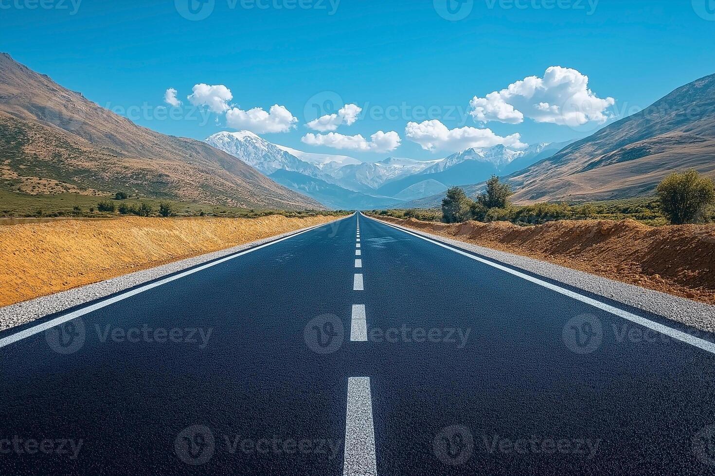 A stunning view of a long, straight road stretching through beautiful mountainous terrain under a vibrant blue sky. photo