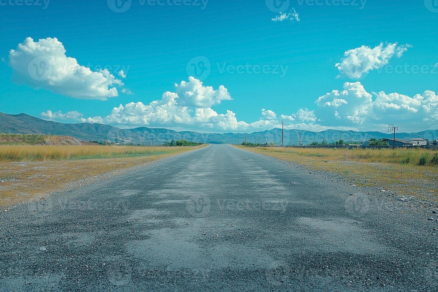 A serene rural road stretches into the horizon under a vibrant blue sky filled with fluffy white clouds. photo