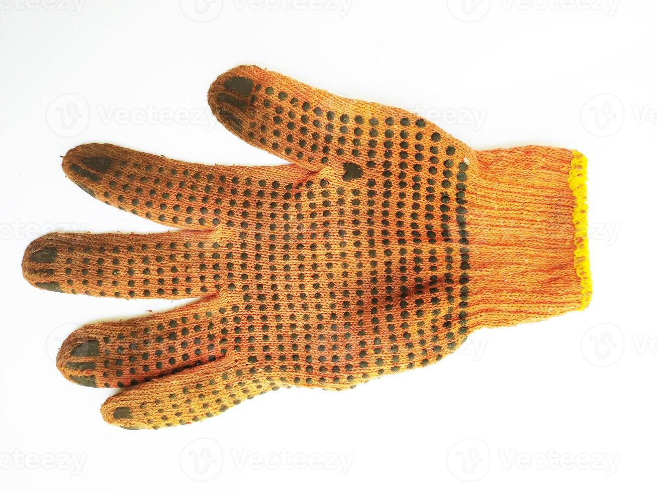 A wellworn orange work glove, showcasing its textured surface and darkcolored grip dots, lies against a clean white background. The image evokes themes of hard work, manual labor, and resilience. photo