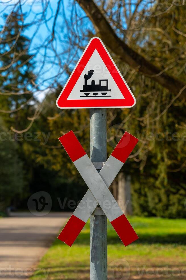 Warning sign alerts pedestrians to nearby railroad tracks and train traffic in a park on a sunny day photo