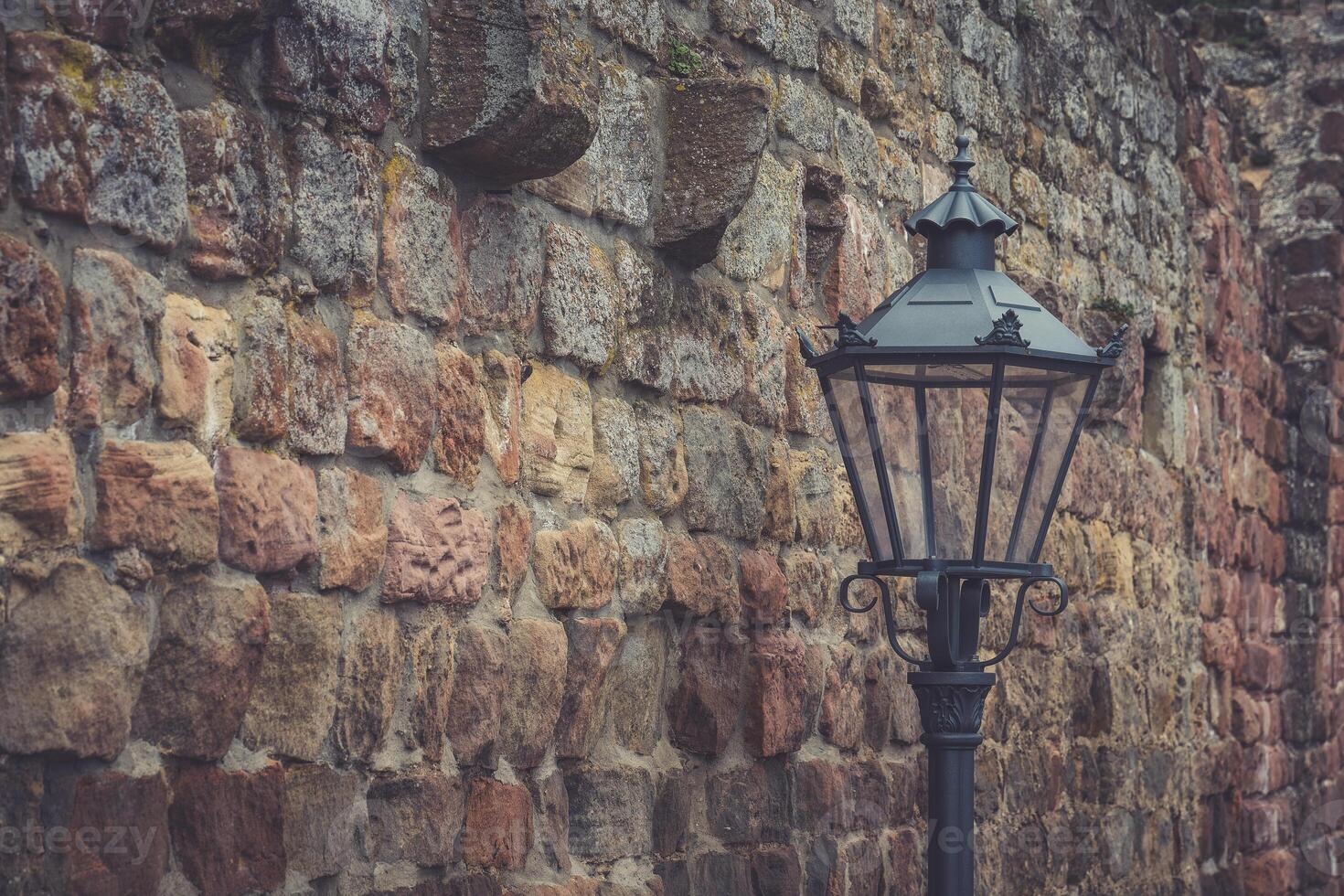Vintage street lamp stands against an ancient stone wall in an old town photo