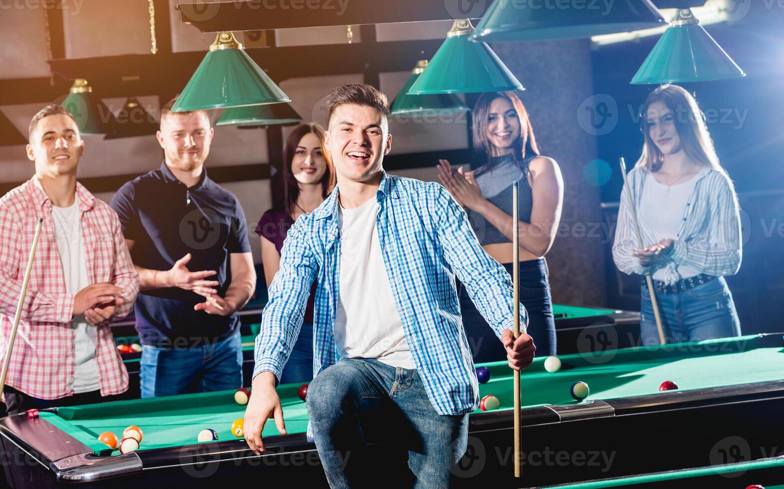 Young man playing in billiard. Posing near the table with a cue in his hands photo