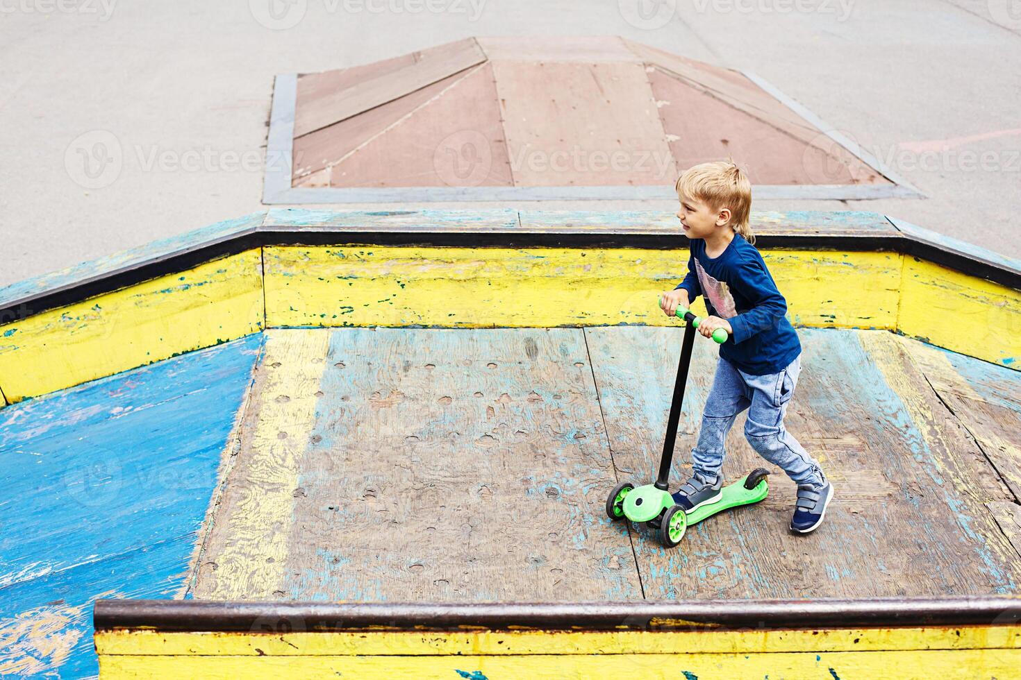 Boy with Kick Scooter Having Fun in Skatepark. Child Making Stunts Enjoying Outdoor Activities. photo