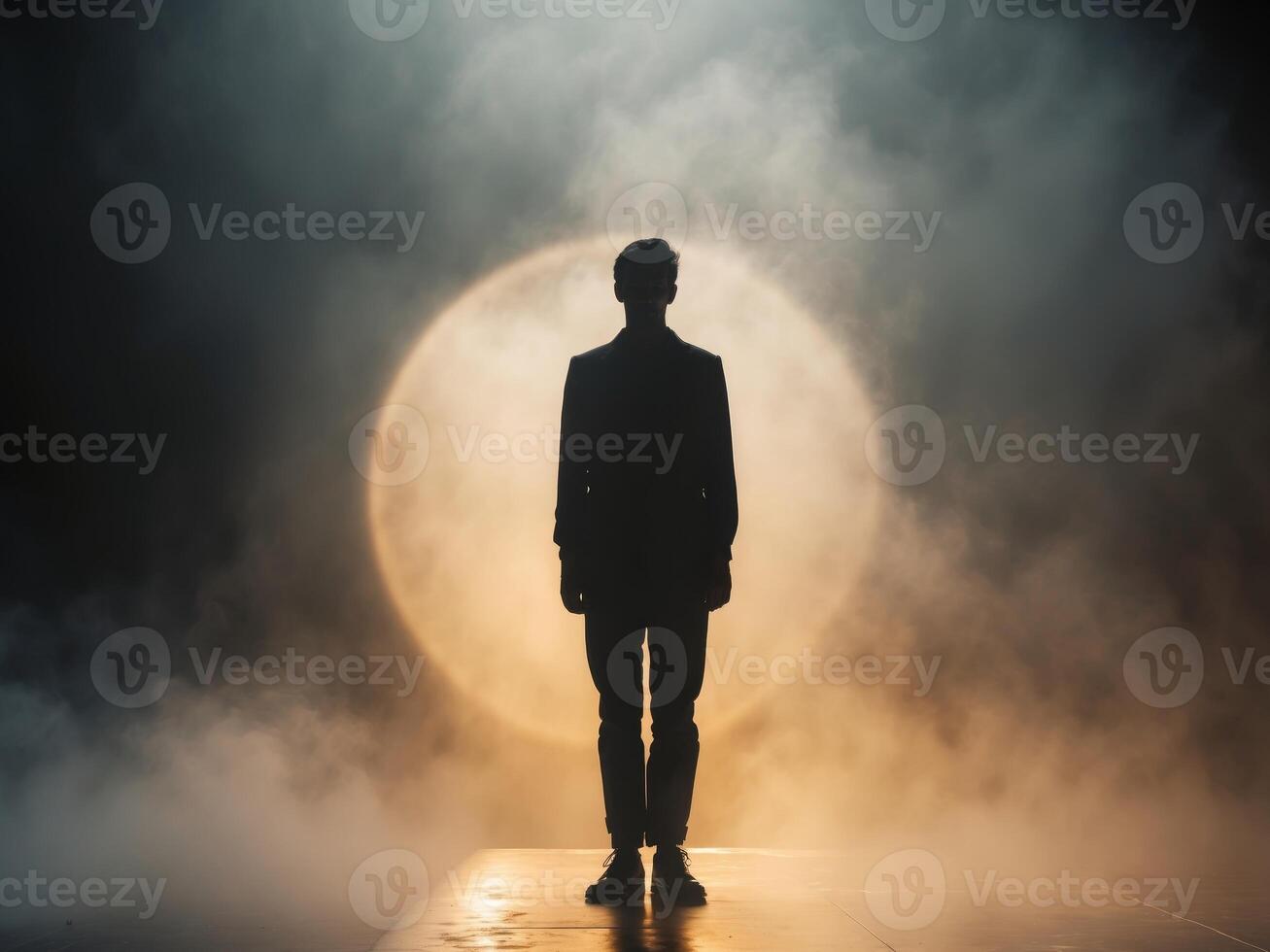 A lone figure stands on a smoky stage illuminated by spotlights photo